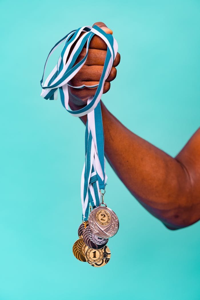 Close-up of a hand holding various medals with blue ribbons against a turquoise background.