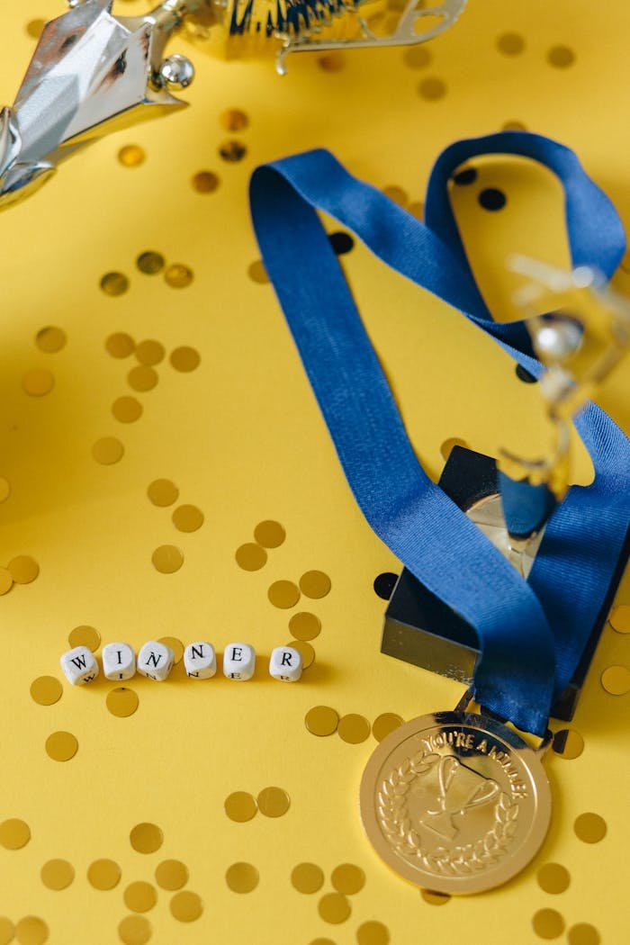 Gold medal and winners trophy on a vibrant yellow confetti background, symbolizing success and victory.